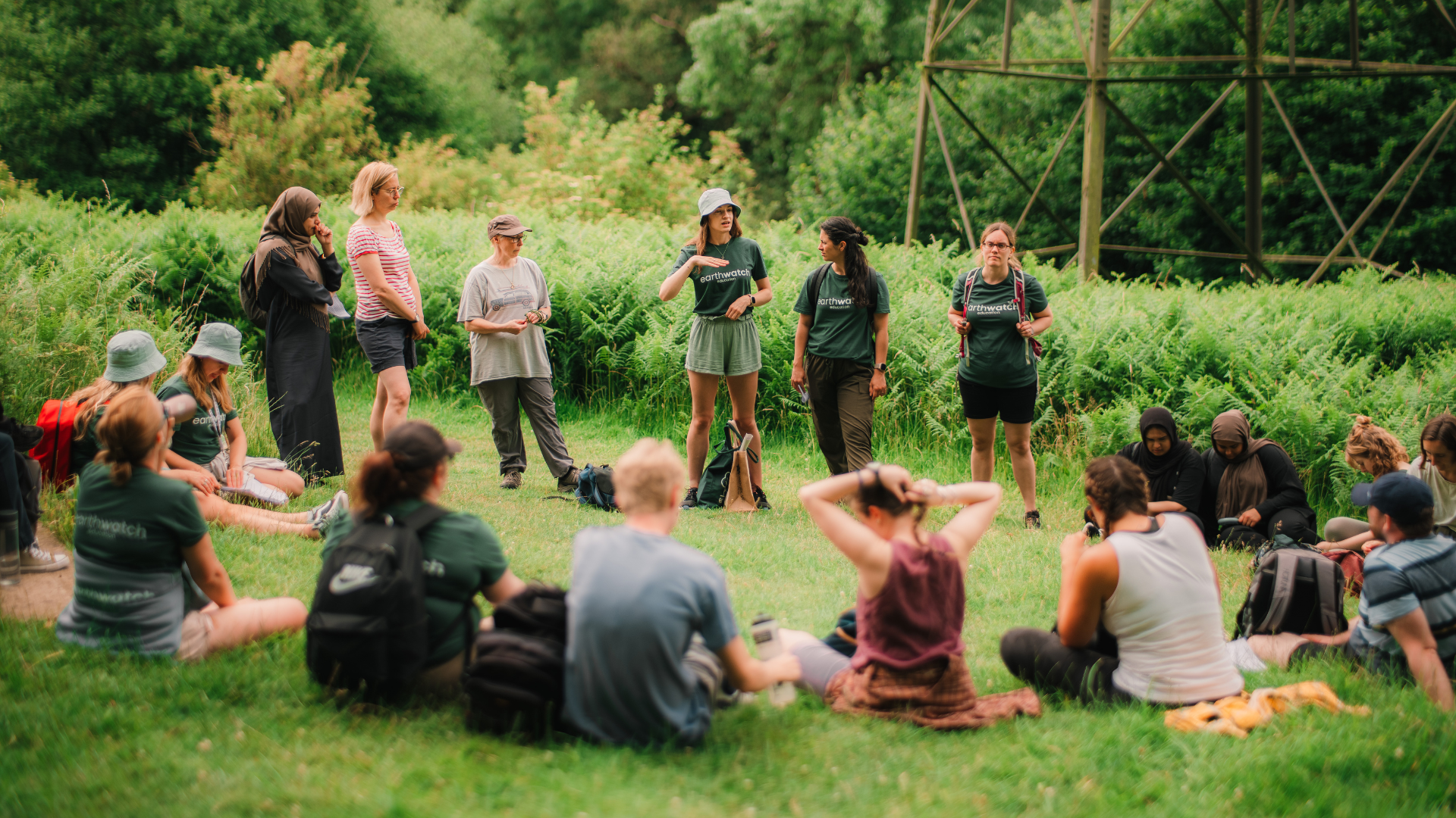 A group of teachers sitting in a circle outside surrounded by nature. Earthwatch Education staff in branded t-shirts giving a presentation.