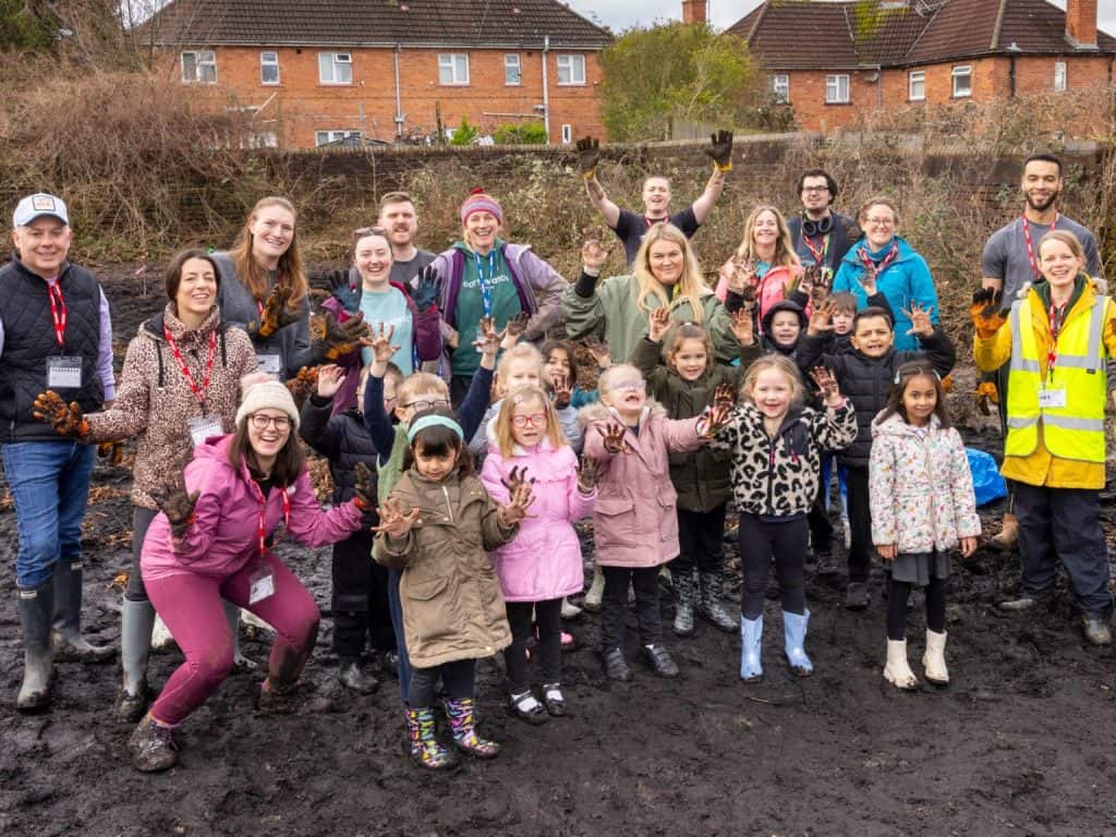 A group of school children with representatives from business and community showing off their very muddy hands at a Tiny Forest planting
