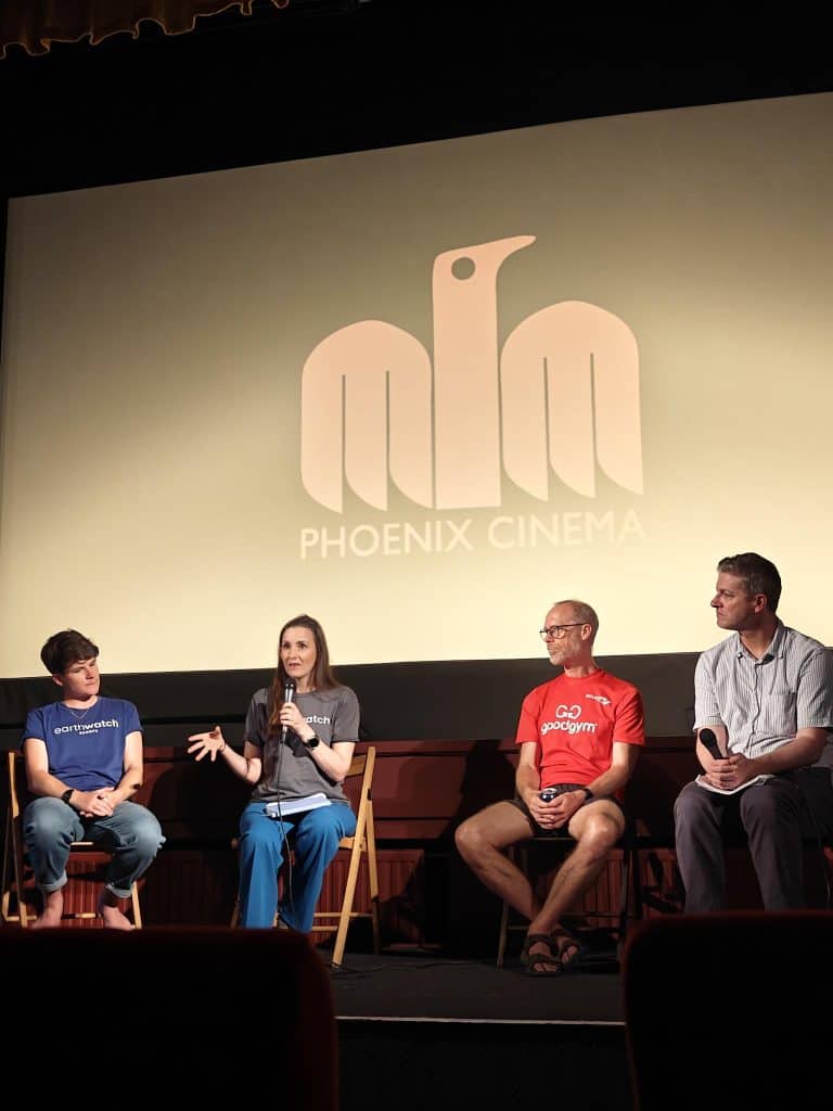 A photograph of the panel QnA following the film screening. Four speakers sit on chairs facing the audience and hold microphones.